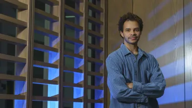 Cameron Merline, male student standing in front of decorative wall divider